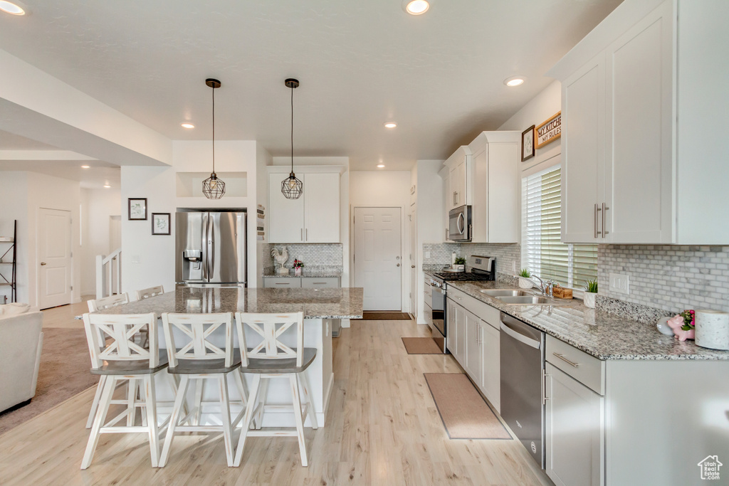 Kitchen with appliances with stainless steel finishes, a breakfast bar, a center island, light wood-type flooring, and a sink