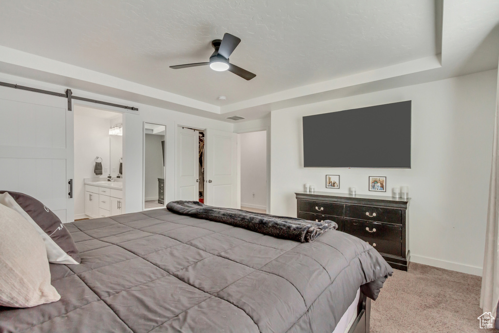 Carpeted bedroom with a tray ceiling, ensuite bath, baseboards, and a barn door