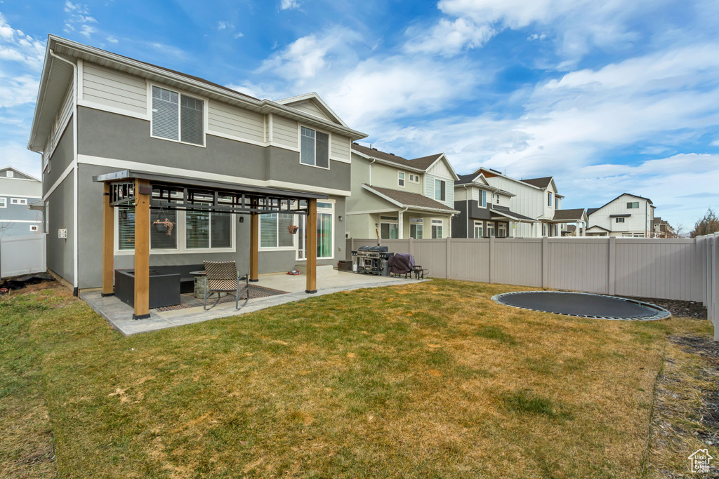 Back of property featuring a patio area, a fenced backyard, a trampoline, and a yard