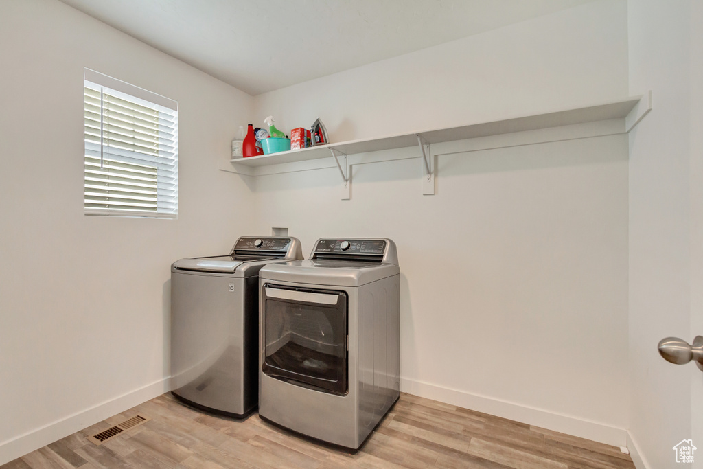 Washroom with washer and clothes dryer, visible vents, light wood-type flooring, laundry area, and baseboards