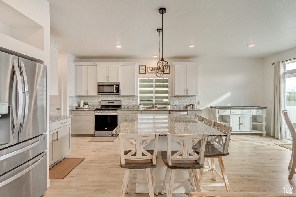 Kitchen featuring appliances with stainless steel finishes, light wood-type flooring, white cabinetry, and decorative backsplash