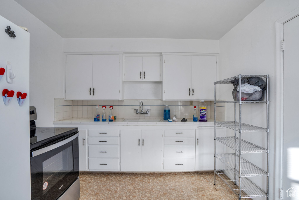 Kitchen featuring tasteful backsplash, tile counters, electric stove, and white cabinetry