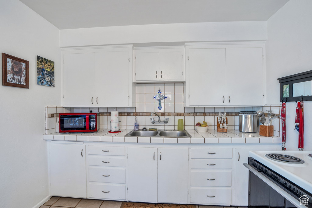 Kitchen featuring light tile patterned floors, a sink, white cabinetry, tile counters, and tasteful backsplash