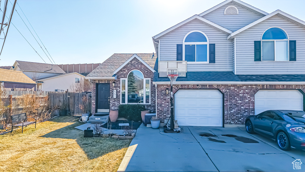 Traditional home featuring concrete driveway, brick siding, fence, and a front lawn