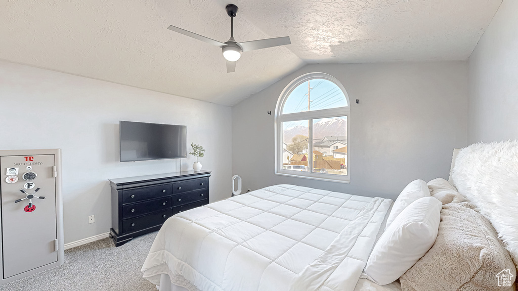 Bedroom featuring a ceiling fan, light carpet, vaulted ceiling, a textured ceiling, and baseboards