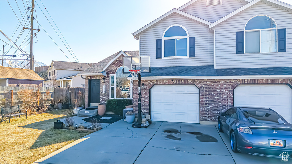 View of front facade with driveway, roof with shingles, an attached garage, fence, and brick siding