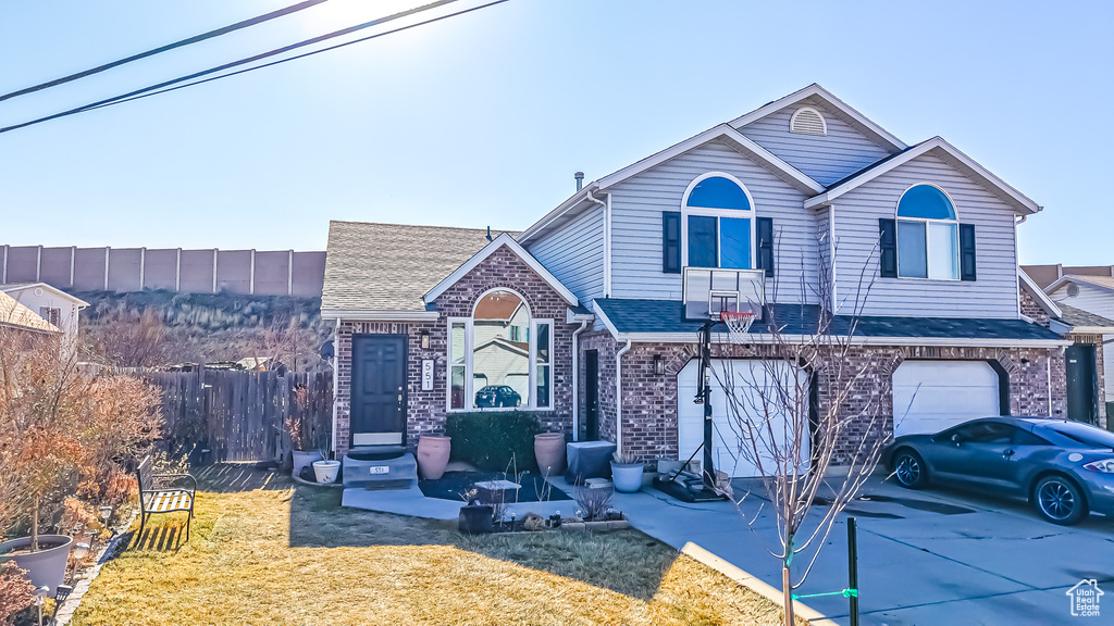 Traditional-style house featuring driveway, a garage, fence, a front lawn, and brick siding