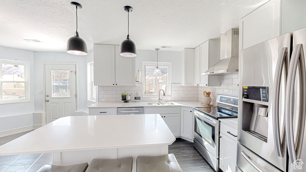 Kitchen featuring stainless steel appliances, light countertops, backsplash, a sink, and wall chimney exhaust hood