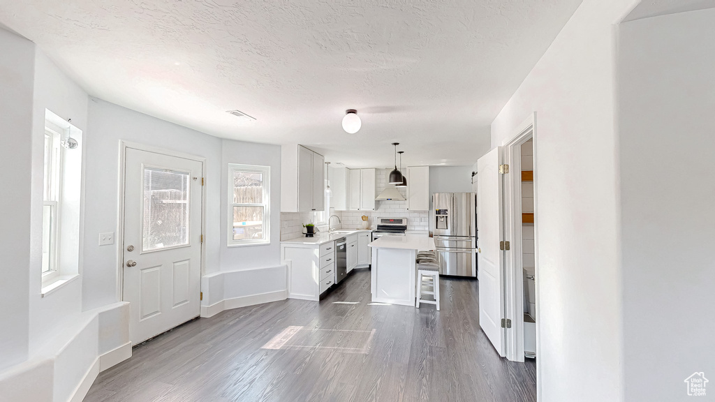 Kitchen with a breakfast bar, decorative backsplash, appliances with stainless steel finishes, white cabinets, and wall chimney range hood