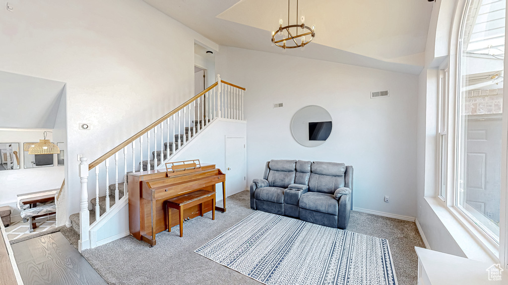 Living area with high vaulted ceiling, visible vents, stairway, a chandelier, and baseboards