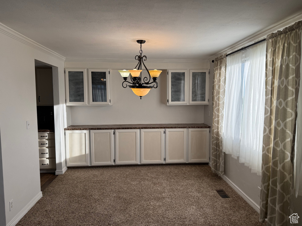 Unfurnished dining area with a chandelier, dark carpet, baseboards, and ornamental molding