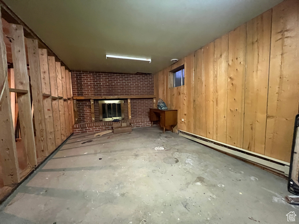 Finished basement with wood walls, a baseboard radiator, and a brick fireplace