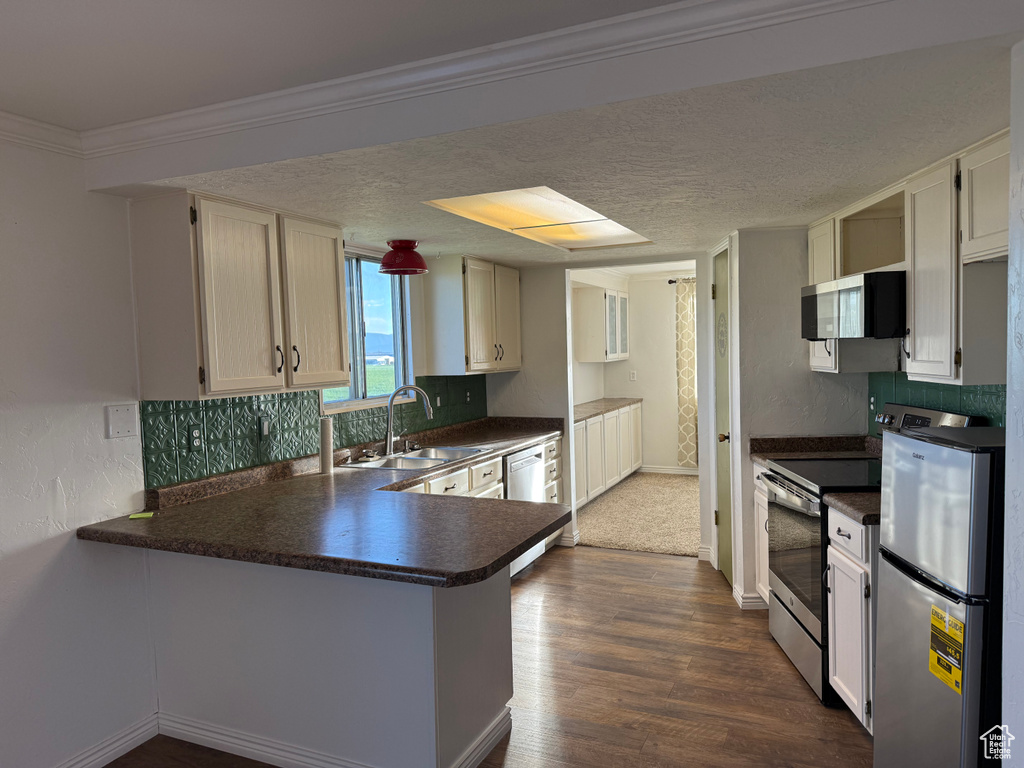 Kitchen featuring a sink, appliances with stainless steel finishes, dark countertops, a peninsula, and a textured ceiling