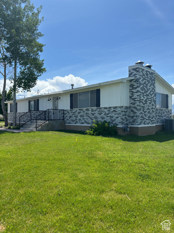 View of front facade featuring central air condition unit, board and batten siding, and a front lawn
