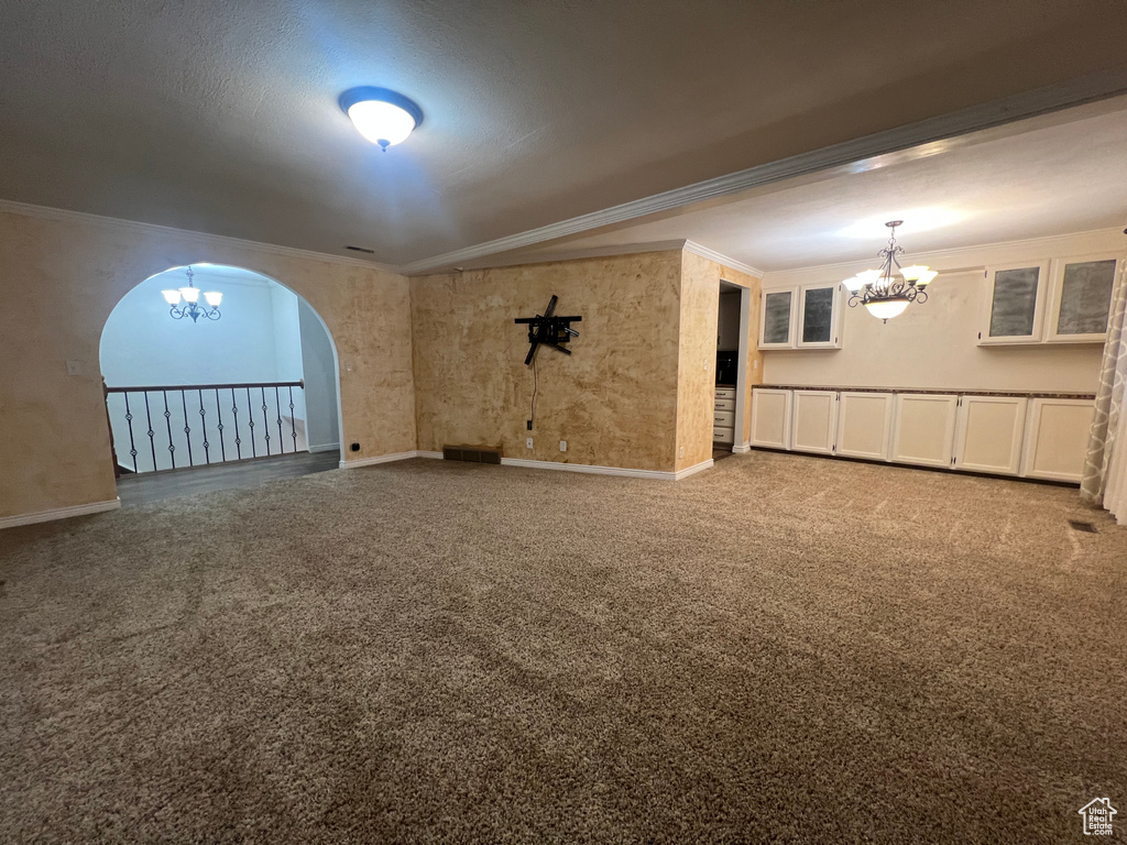 Carpeted spare room featuring arched walkways, ornamental molding, baseboards, and a notable chandelier