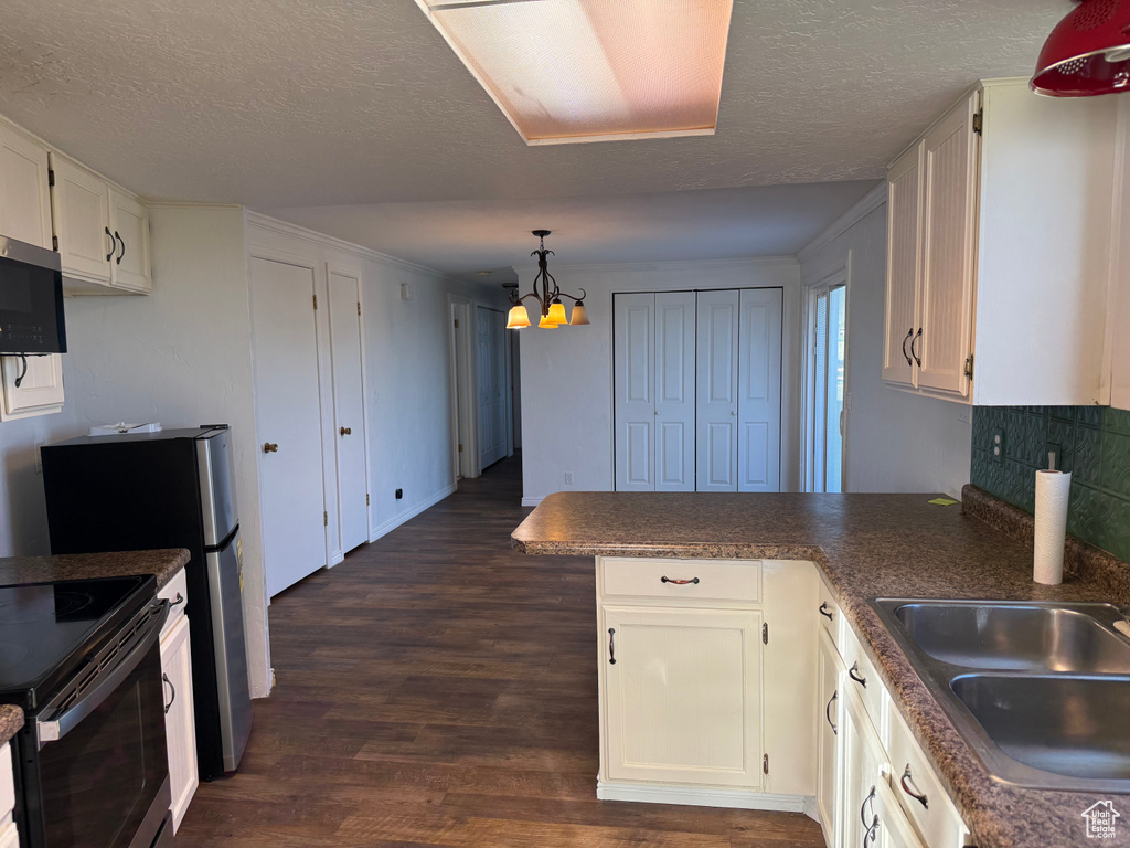 Kitchen featuring a peninsula, a chandelier, dark wood-style floors, white cabinets, and stainless steel microwave