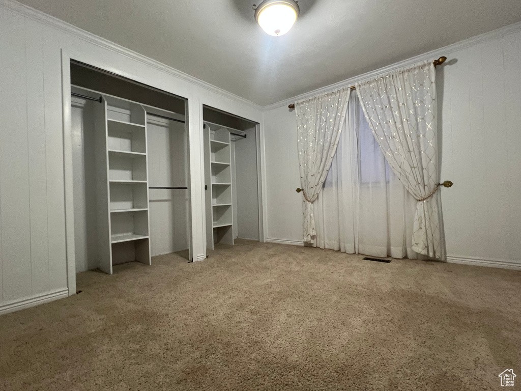 Unfurnished bedroom featuring wooden walls, carpet flooring, visible vents, multiple closets, and crown molding