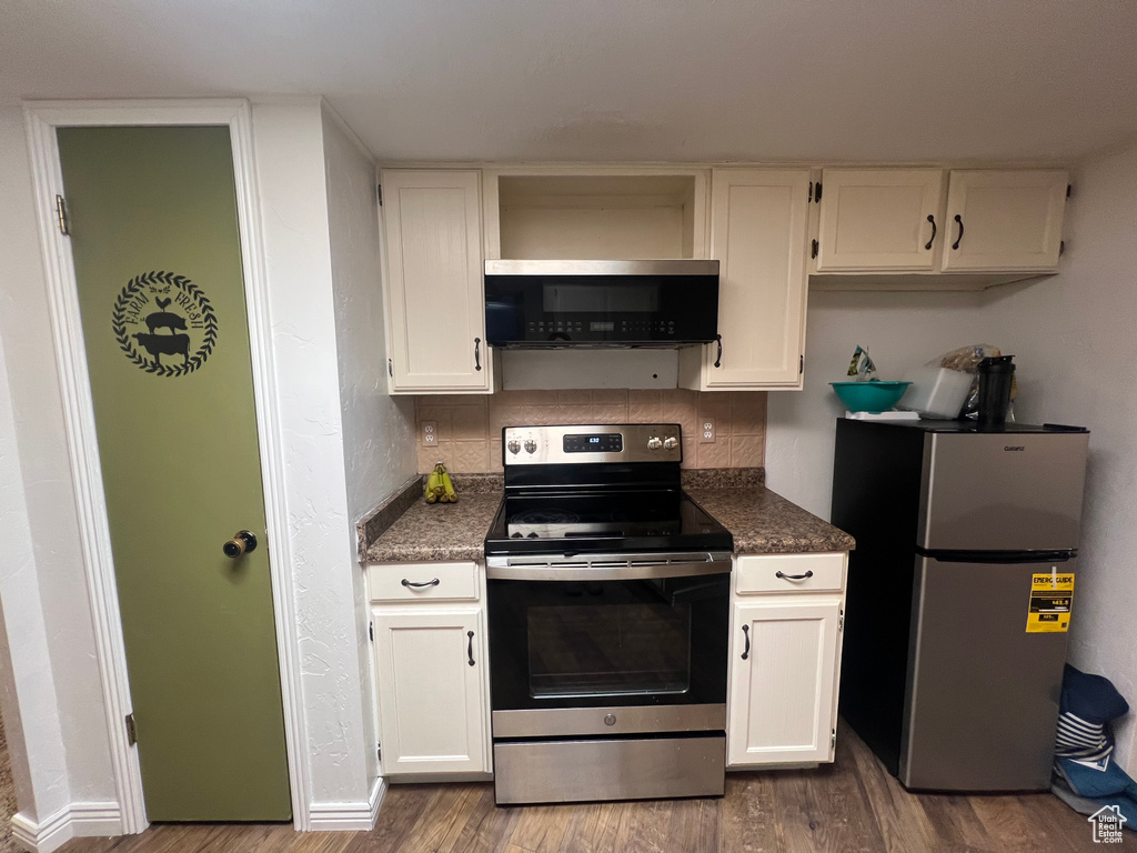 Kitchen featuring stainless steel appliances, dark countertops, white cabinetry, and wood finished floors