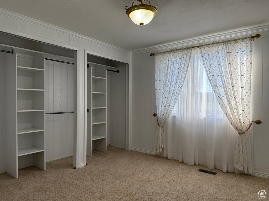 Unfurnished bedroom featuring ornamental molding, carpet floors, and two closets