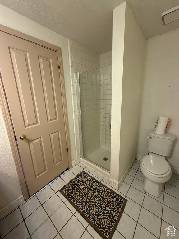 Full bathroom featuring tile patterned flooring, toilet, a shower stall, baseboards, and a textured ceiling