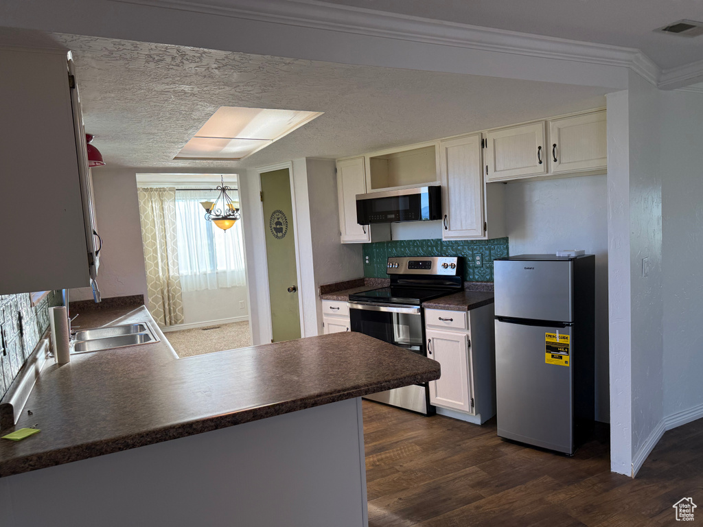Kitchen with appliances with stainless steel finishes, dark countertops, a sink, dark wood-type flooring, and crown molding