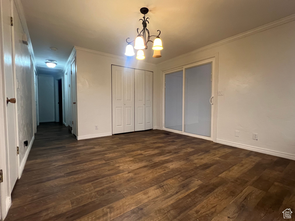 Unfurnished bedroom featuring a notable chandelier, ornamental molding, dark wood finished floors, and baseboards