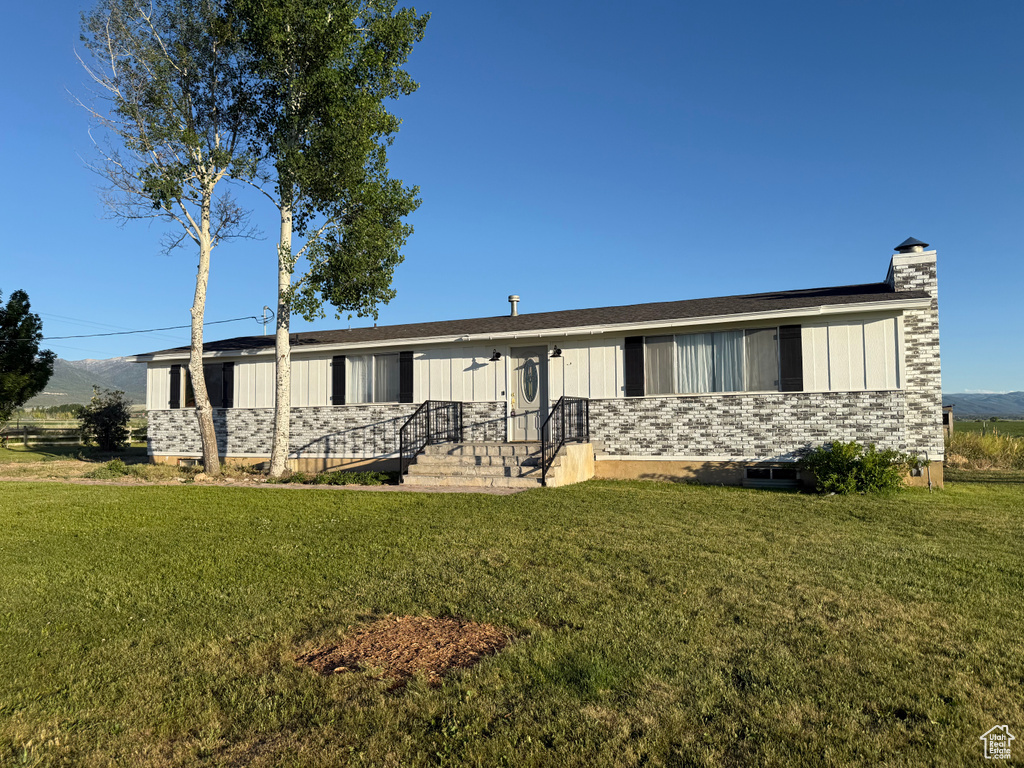 Ranch-style home featuring a front lawn, a chimney, and board and batten siding