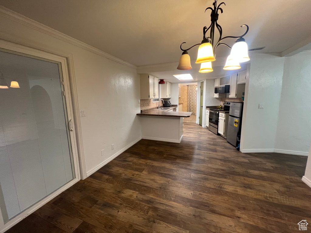 Kitchen with baseboards, appliances with stainless steel finishes, ornamental molding, dark wood-style flooring, and a peninsula