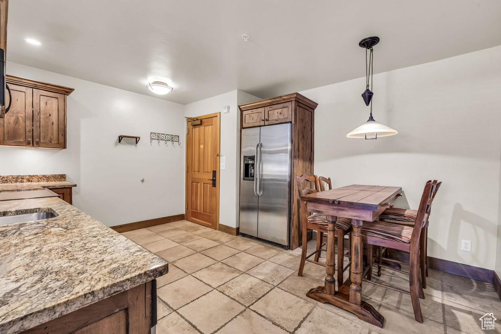 Kitchen with stainless steel fridge with ice dispenser, hanging light fixtures, light tile patterned flooring, and light stone counters