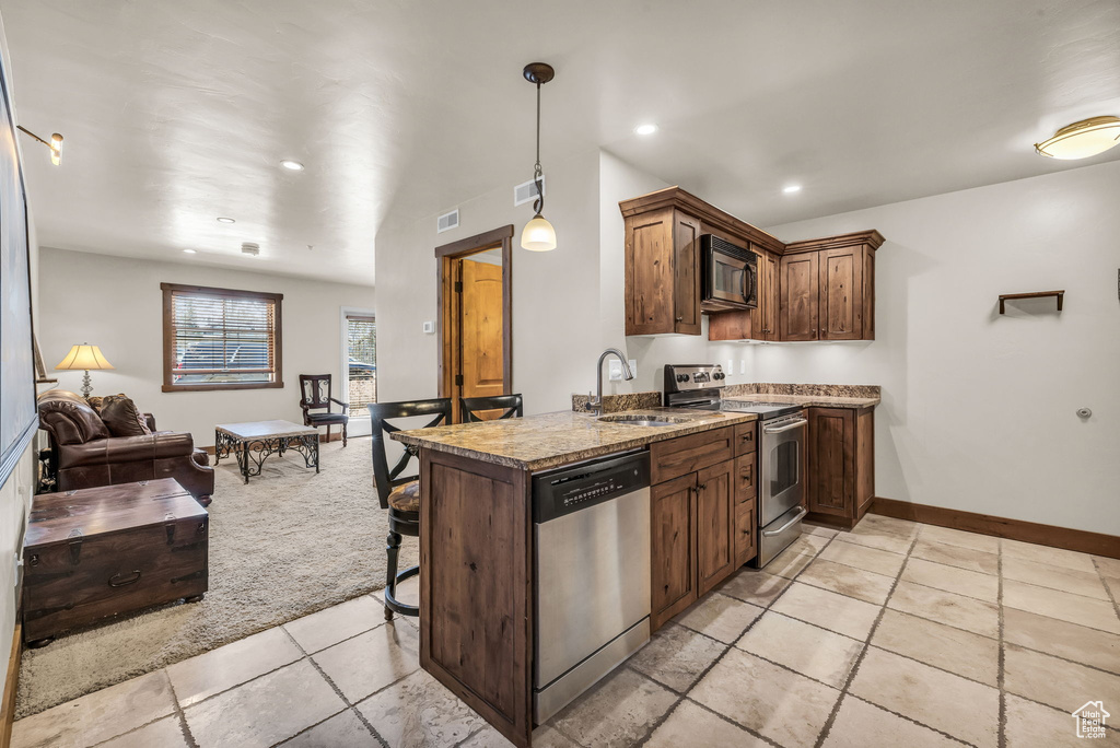 Kitchen featuring stainless steel appliances, recessed lighting, pendant lighting, a kitchen bar, and open floor plan