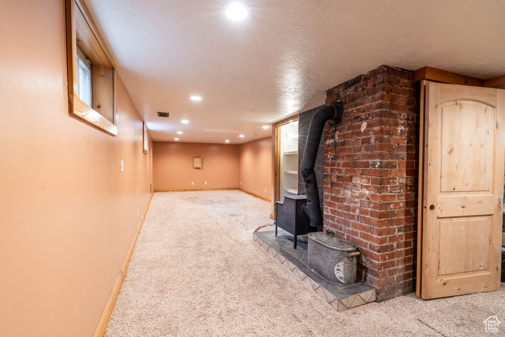 Unfurnished living room featuring light carpet, a textured ceiling, and a wood stove