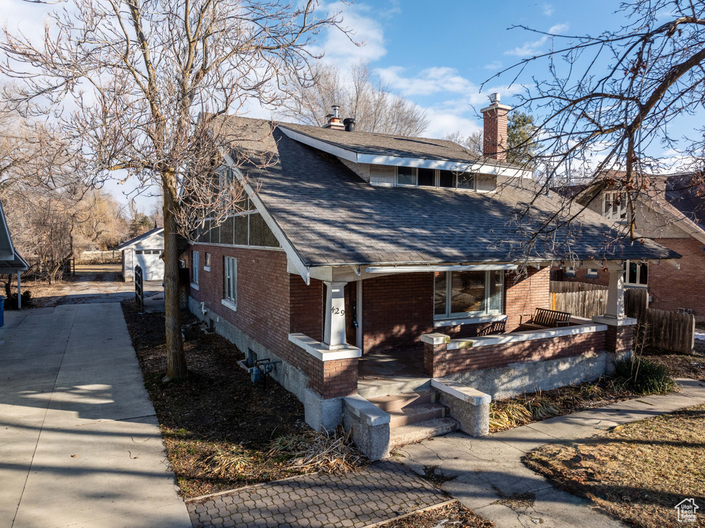 View of front of home featuring an outbuilding, brick siding, a chimney, and roof with shingles