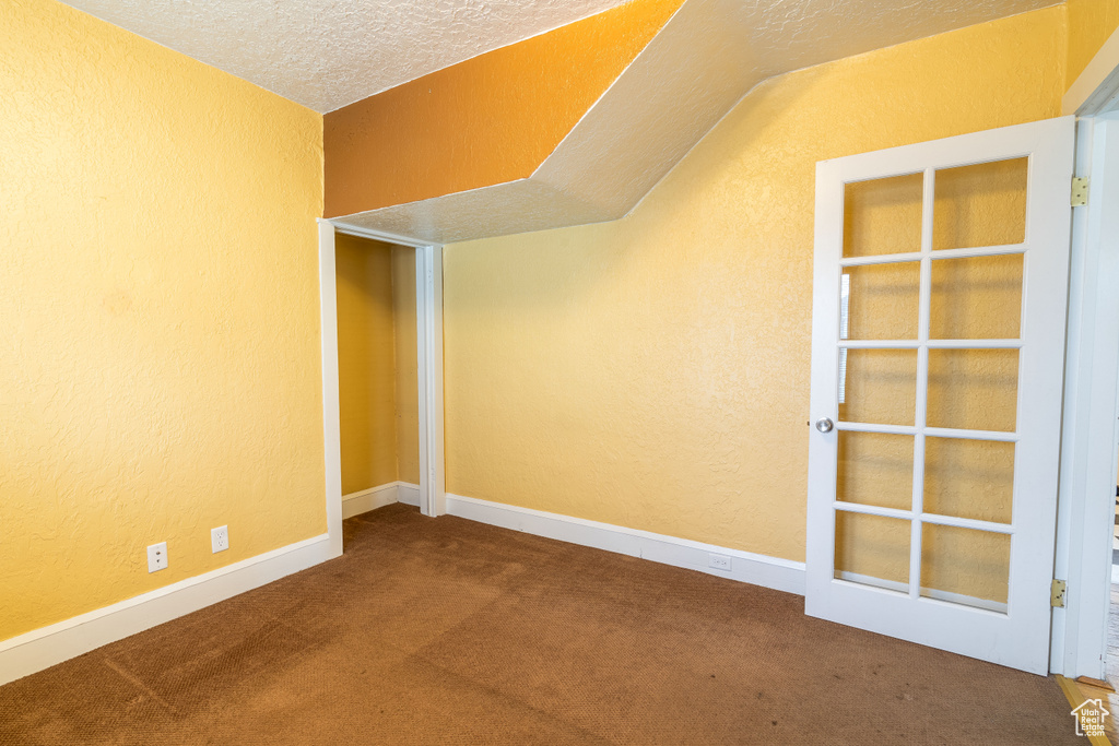 Carpeted empty room featuring vaulted ceiling and a textured ceiling