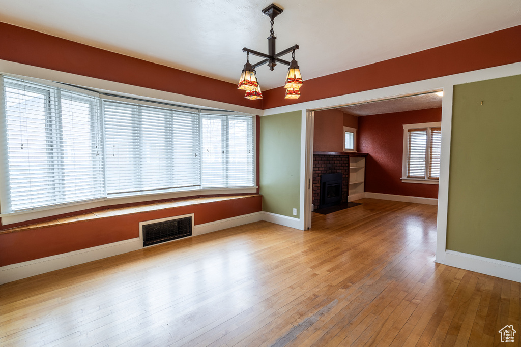 Unfurnished living room featuring hardwood / wood-style flooring, a healthy amount of sunlight, and a brick fireplace