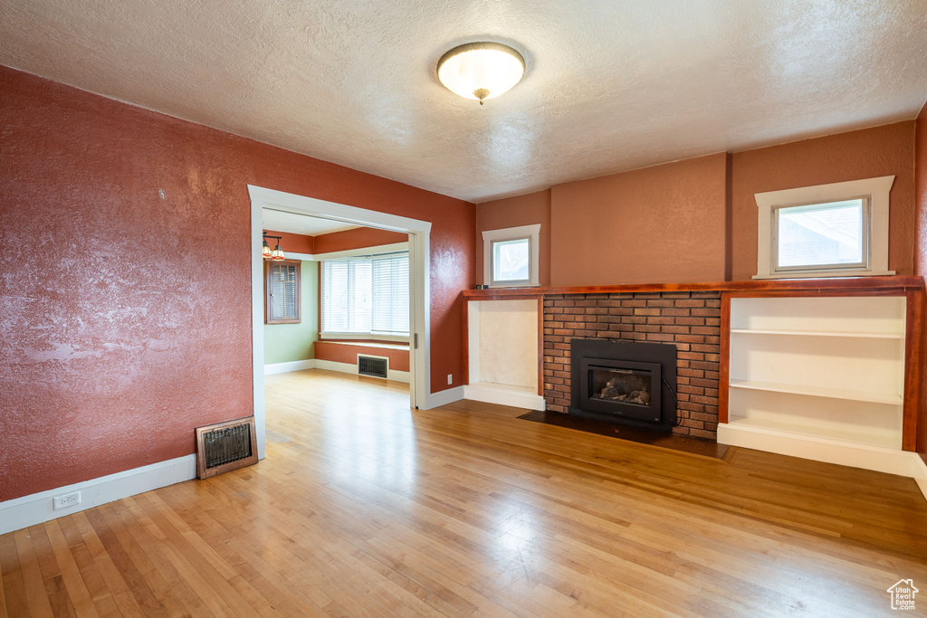 Unfurnished living room featuring a brick fireplace, a textured ceiling, and light wood-type flooring