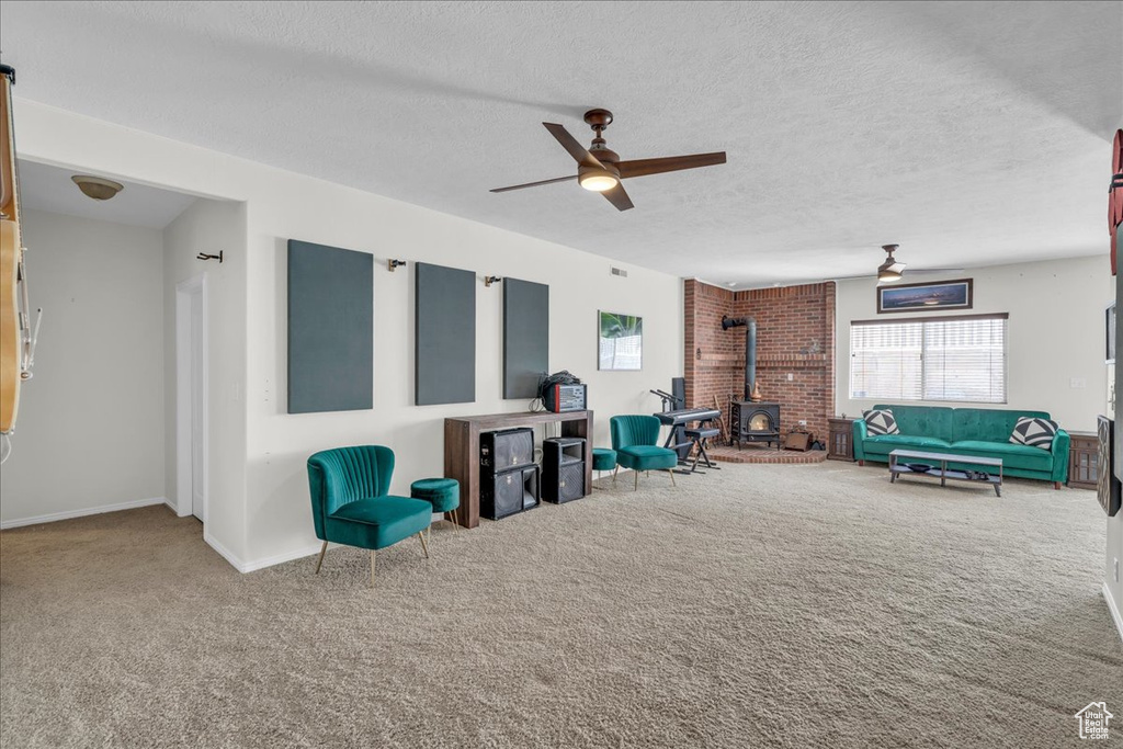 Living area with a wood stove, a ceiling fan, carpet flooring, and a textured ceiling
