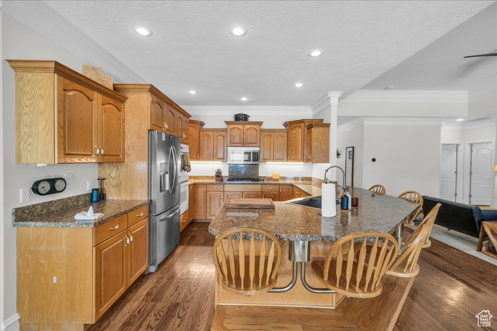 Kitchen with appliances with stainless steel finishes, a sink, a kitchen breakfast bar, dark wood-style flooring, and crown molding