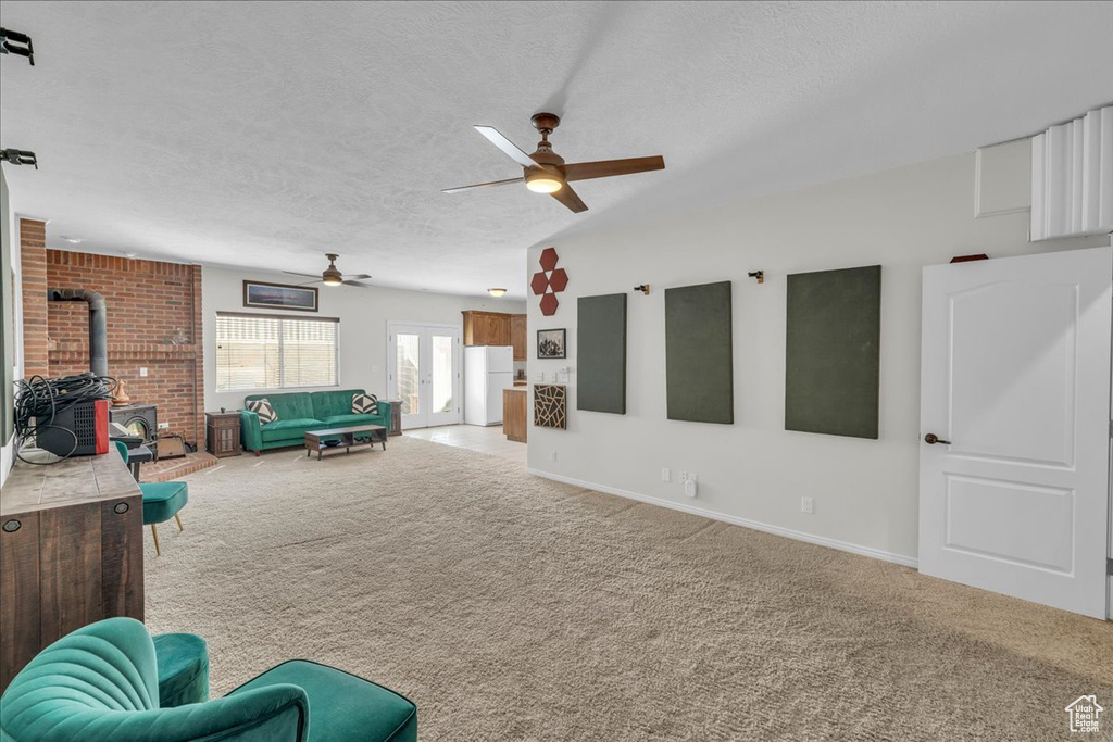 Living area featuring a textured ceiling, ceiling fan, light carpet, a wood stove, and baseboards