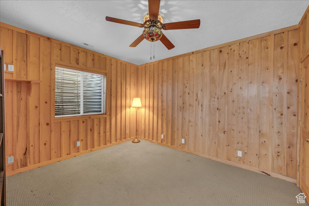 Carpeted spare room featuring ceiling fan, wood walls, and baseboards
