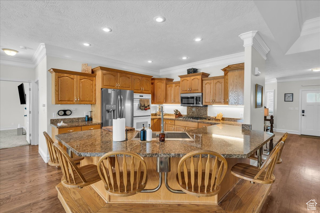 Kitchen featuring appliances with stainless steel finishes, ornamental molding, baseboards, a breakfast bar area, and brown cabinetry