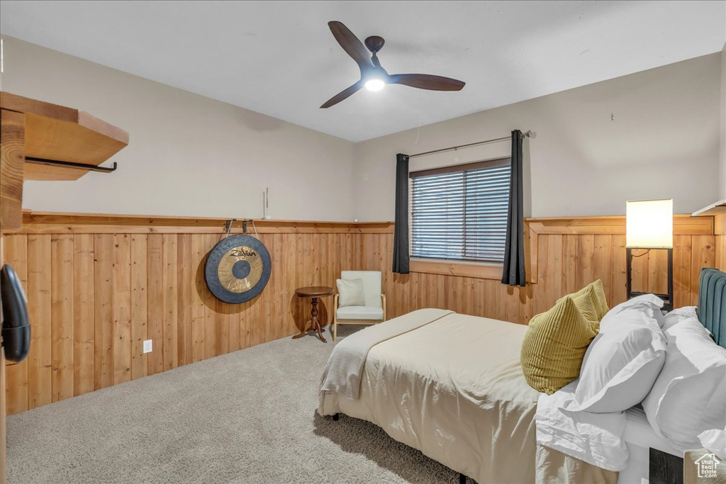 Carpeted bedroom with wooden walls, wainscoting, and a ceiling fan