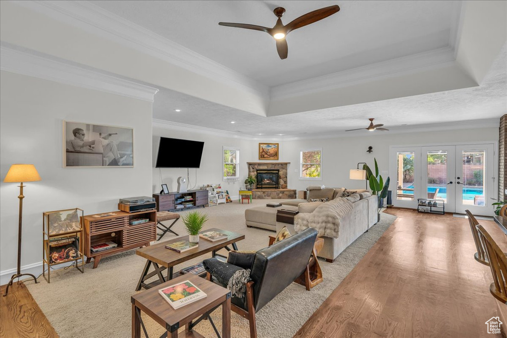 Living area with a ceiling fan, french doors, wood finished floors, a tray ceiling, and crown molding