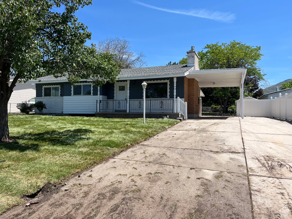 View of front facade featuring a porch, driveway, a chimney, an attached carport, and roof with shingles