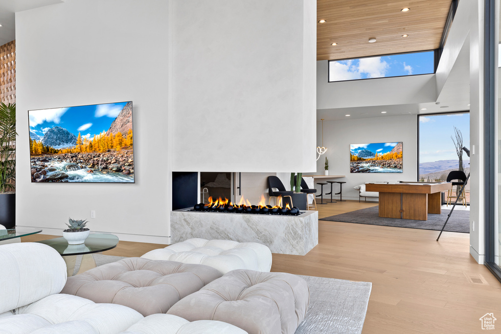 Living room with recessed lighting, a high ceiling, wood ceiling, wood finished floors, and a multi sided fireplace