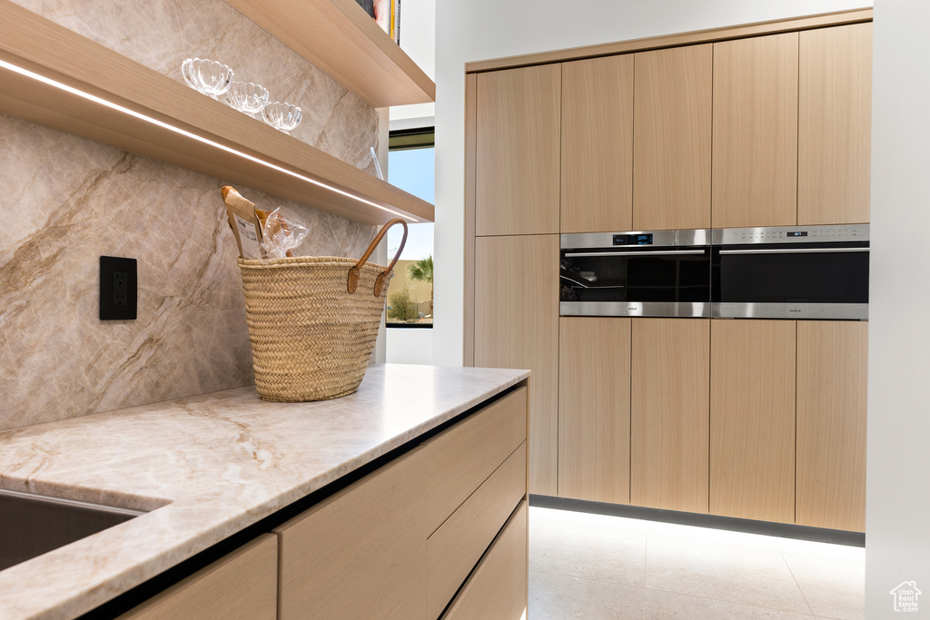 Kitchen with open shelves, modern cabinets, backsplash, stainless steel double oven, and light stone countertops