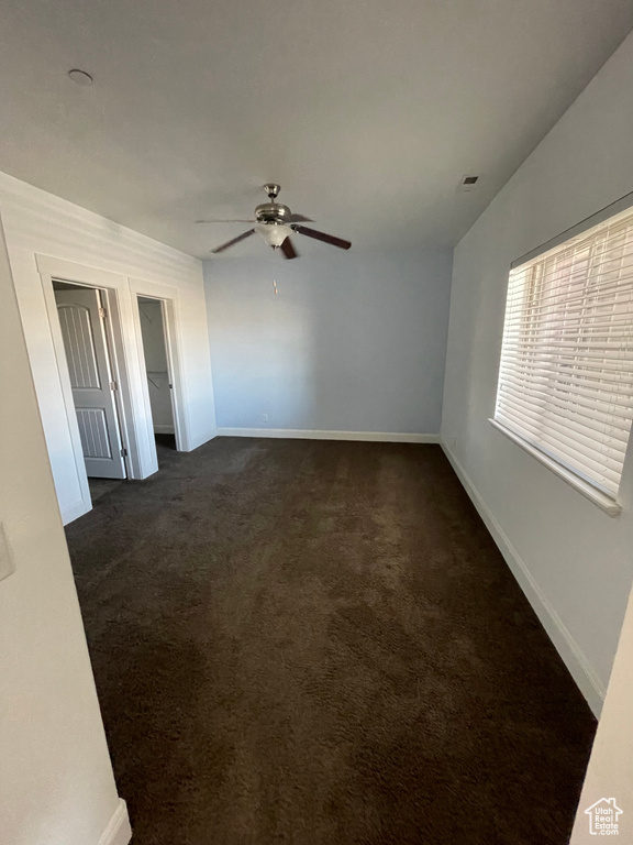 Empty room featuring dark carpet, baseboards, and ceiling fan