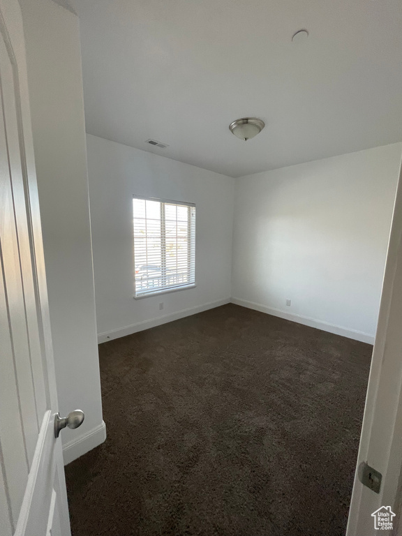 Spare room with dark colored carpet, visible vents, and baseboards