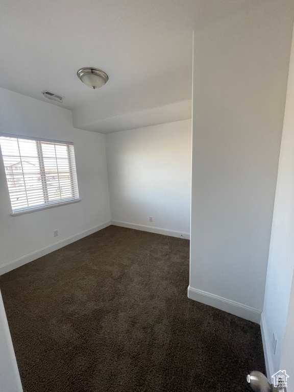 Empty room featuring dark carpet, visible vents, and baseboards