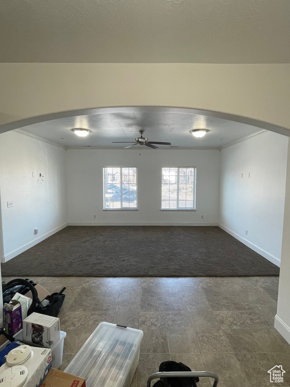 Carpeted spare room featuring a ceiling fan, arched walkways, and baseboards