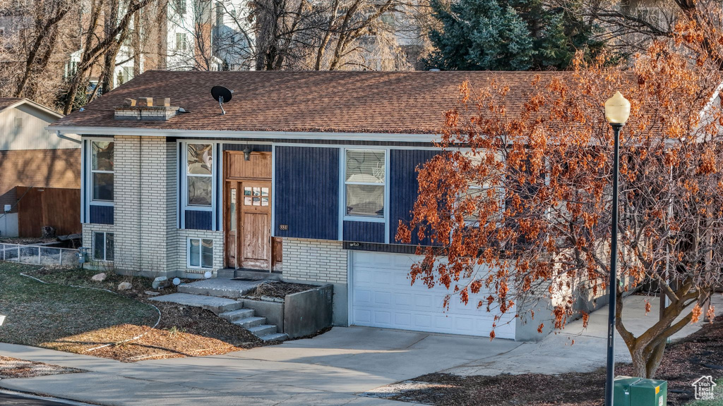 View of front of property featuring an attached garage, driveway, a shingled roof, and brick siding